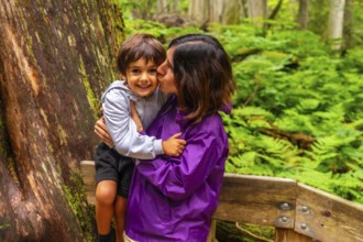 Mother kissing her smiling son while hiking the giant cedars boardwalk trail in mount revelstoke