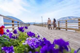 Tourists walking on a wooden pier adorned with vibrant flowers, enjoying the scenic beauty of