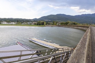 Dragon boats are tied up at a floating dock near a wooden pier, with the city of salmon arm and the
