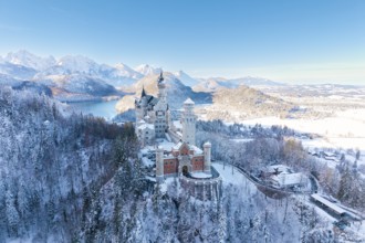 Fairytale castle Neuschwanstein in snowy landscape surrounded by majestic mountains and blue skies,