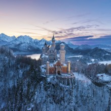 Wintery Neuschwanstein Castle at dusk surrounded by snow-covered mountains, Schwangau near Füssen,