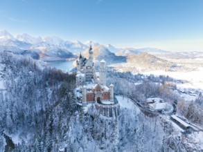 Wintery Neuschwanstein Castle with bright sky, surrounded by snow-capped mountains and forests,