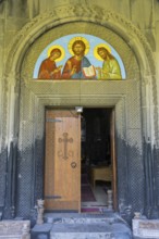 Opened wooden door with religious icon above, embedded in ancient stone decorated arch, Akhtala