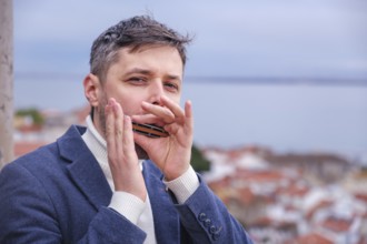 Man musician in a blue blazer and white sweater playing blues on a harmonica with eyes closed,