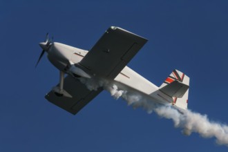 Stunt aerobatic plane performing stunts in blue sky with smoke trail. Concept of speed, difficulty,