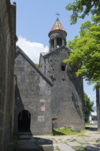Stone church tower with bell tower, surrounded by trees and shade, blue sky visible, Sanahin