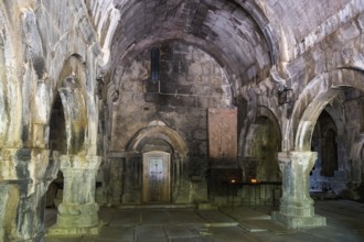 Dark, antique stone hall with arches flanked by glowing candles, Sanahin monastery, Sanahin town,