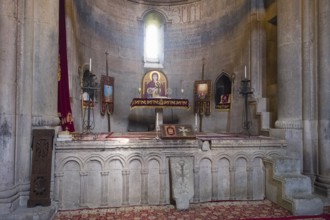Historic church altar with icons and candles in a stone room, illuminated by windows, Goshavank