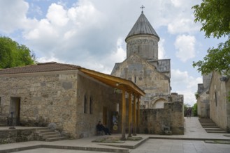 Church building with tower and stone walls, surrounded by trees, in cloudy sky, Haghartsin