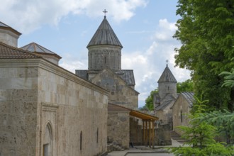 Monastery with stone buildings and towers under partly cloudy sky, surrounded by trees, Haghartsin