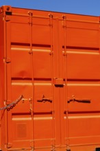 Locked bright fluorescent orange painted metal box shaped shipping container with doors locked
