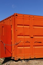 Locked bright fluorescent orange painted metal box shaped shipping container with door kept opened