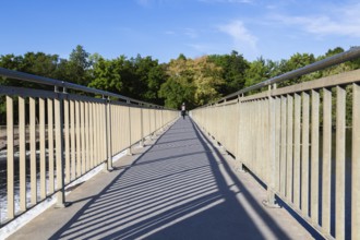 Electric scooter rider on pedestrian walkway on top of water flow control Moulin Neuf dam over Des
