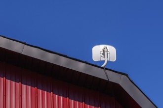 White satellite T.V dish antenna installed on gable roof of building cladded with red sheet metal