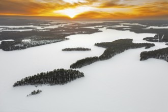 Aerial view over forest and snow covered frozen Lahnaselkä lake in Kuusamo in winter, Koillismaa,