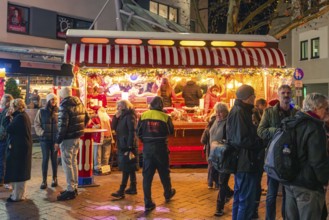 A festively illuminated Christmas market stand with lots of people in a wintry evening mood,