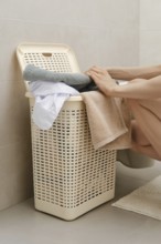 A person is sorting towels and clothes into a laundry basket in a bathroom. The setting is simple,