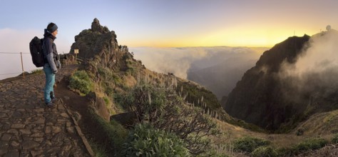 Hiker, woman watching sunrise at Pico do Arieiro, clouds of fog sweeping over mountain peaks, sea