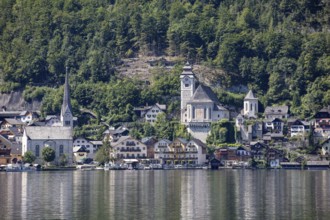 A, Hallstatt, A picturesque village with a lakeside church against a wooded mountain backdrop,