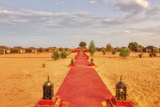 Red carpet trail in the desert, lined with lanterns, leading to tents, Sahara, Morocco