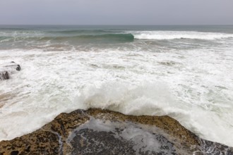 Waves crash over rocks on a grey coast