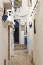 Narrow alley with white buildings, blue decorations, quiet atmosphere