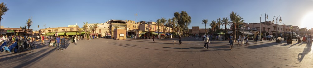 Panoramic view of a town square with shops and palm trees at sunset