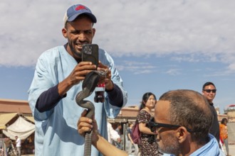 Man photographs a snake on another man's arm in front of an audience