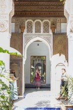 A traditional courtyard with arches, mirrors and decoration and two woman, Bahia Palace in
