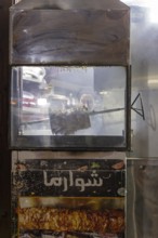 A rotisserie with meat in an illuminated shop window of a restaurant