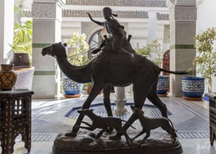Statue of a camel with rider surrounded by traditional decor in a courtyard