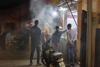 Nocturnal street scene with people, smoke from cooking areas and scooters in a busy area