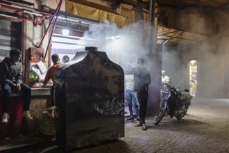 A busy street scene at night with people and smoke in an urban area