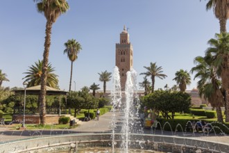 A well-kept garden with a sparkling fountain in front of the majestic Koutoubia Mosque on a sunny