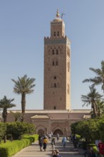 The towering minaret of the Koutoubia Mosque in Marrakech, surrounded by palm trees and visitors in