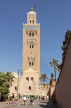 Frontal view of Koutoubia Mosque with passers-by and palm trees in the foreground