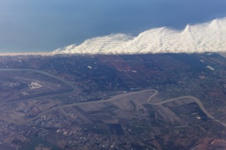 Aerial view of a coastal landscape with waves, agricultural fields and an airport