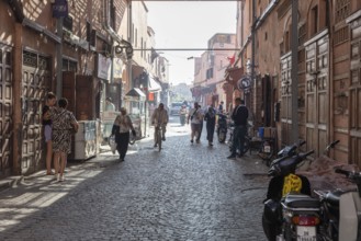Narrow alley with cobblestones and people under bright sunlight