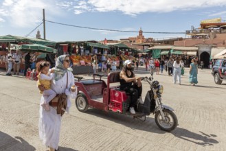 Different people and a man on a scooter on a busy street