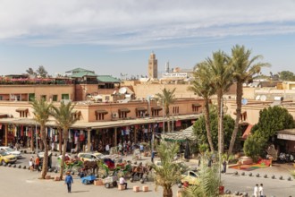 Market scene with palm trees, traditional buildings and a minaret in bright sunshine
