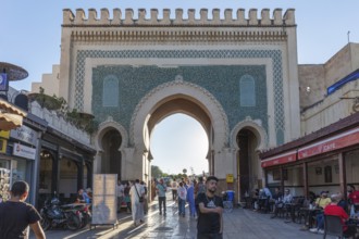 Historic gate with mosaics, people strolling along shops