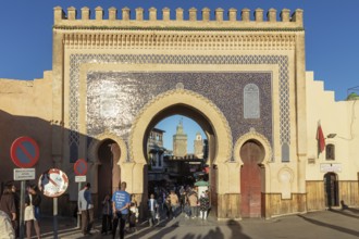 Historic gate with mosaic patterns surrounded by people in daylight