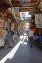 Lively market alleyway with people and traditional stalls in bright light