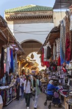 Bustling market corridor with numerous clothes and fabrics under an archway