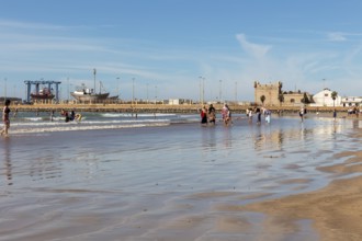 People walking and playing on a city beach under a blue sky
