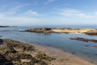 Open coastal landscape with calm sea, rocks and beach under blue sky