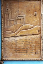 Wood carving with river landscape, sun and buildings framed in blue, traditional door design