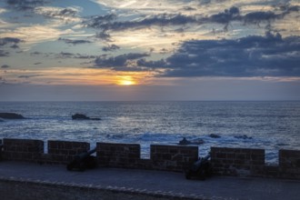 Sunset over the sea with a view of an ancient fortification wall and clouds