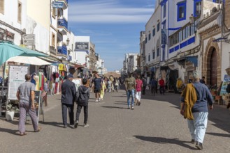 Bustling market street with people and numerous shops under a clear blue sky