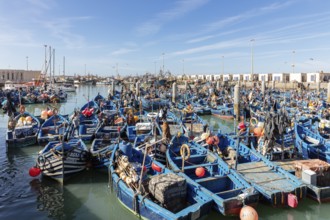 Numerous blue fishing boats close together in the harbor, lively atmosphere under sunny skies